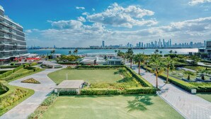 A modern hotel with a landscaped courtyard, a view of the city skyline, and a body of water in the background. - PVH - The8 - Opulent 3BR - Beach Access (Dubai)