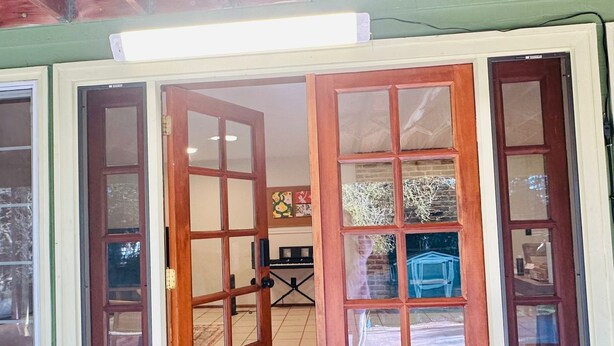 Una porta in legno con un vetrino, un tappetino d'ingresso e, attraverso il vetro, si intravedono un pianoforte e una poltrona blu.