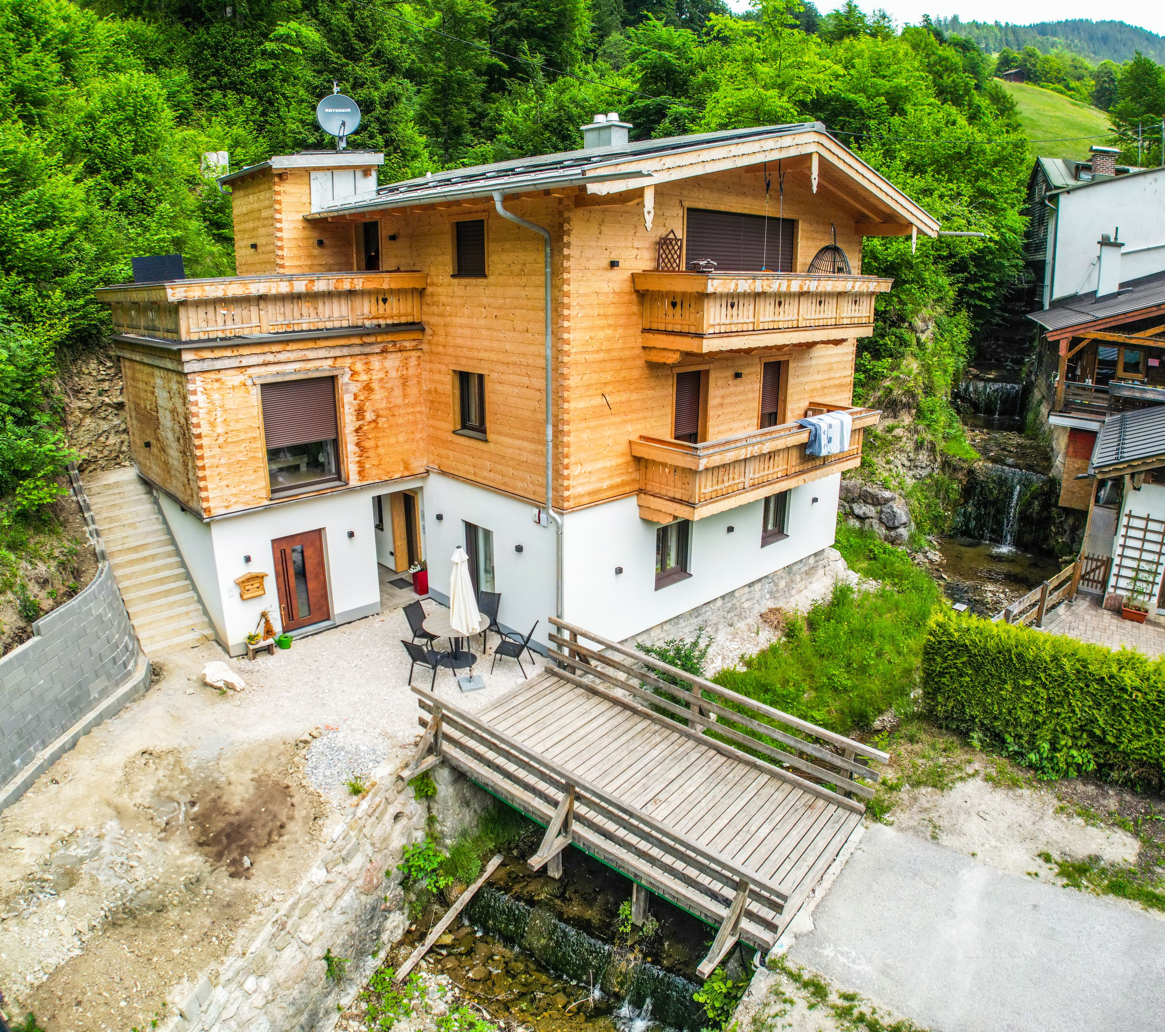 A two-story wooden house with a balcony, a small deck, and a view of a waterfall.