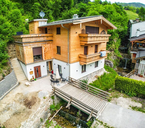 A two-story wooden house with a balcony, a small deck, and a view of a waterfall.