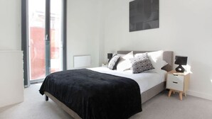 A modern bedroom with a large bed, a nightstand, a lamp, a ceiling light, and a view through a sliding glass door. - The Central Mount-Balcony-Gym-Parking (Manchester)