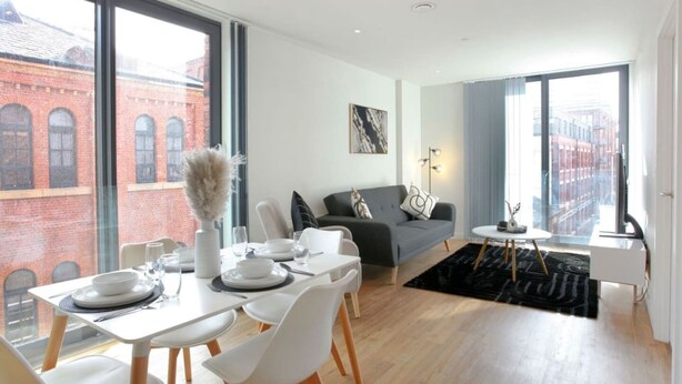 A modern dining area with a table set for four, a grey sofa, and a black rug. - The Central Mount-Balcony-Gym-Parking (Manchester)