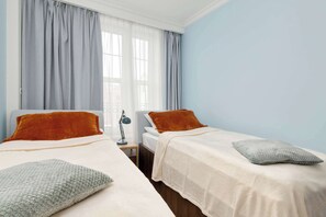 A twin bedroom with two beds, each with a pillow and a bedside table with a lamp. - Elegant Apartment in the Heart of Gdansk | Two Bedrooms (Gdańsk)