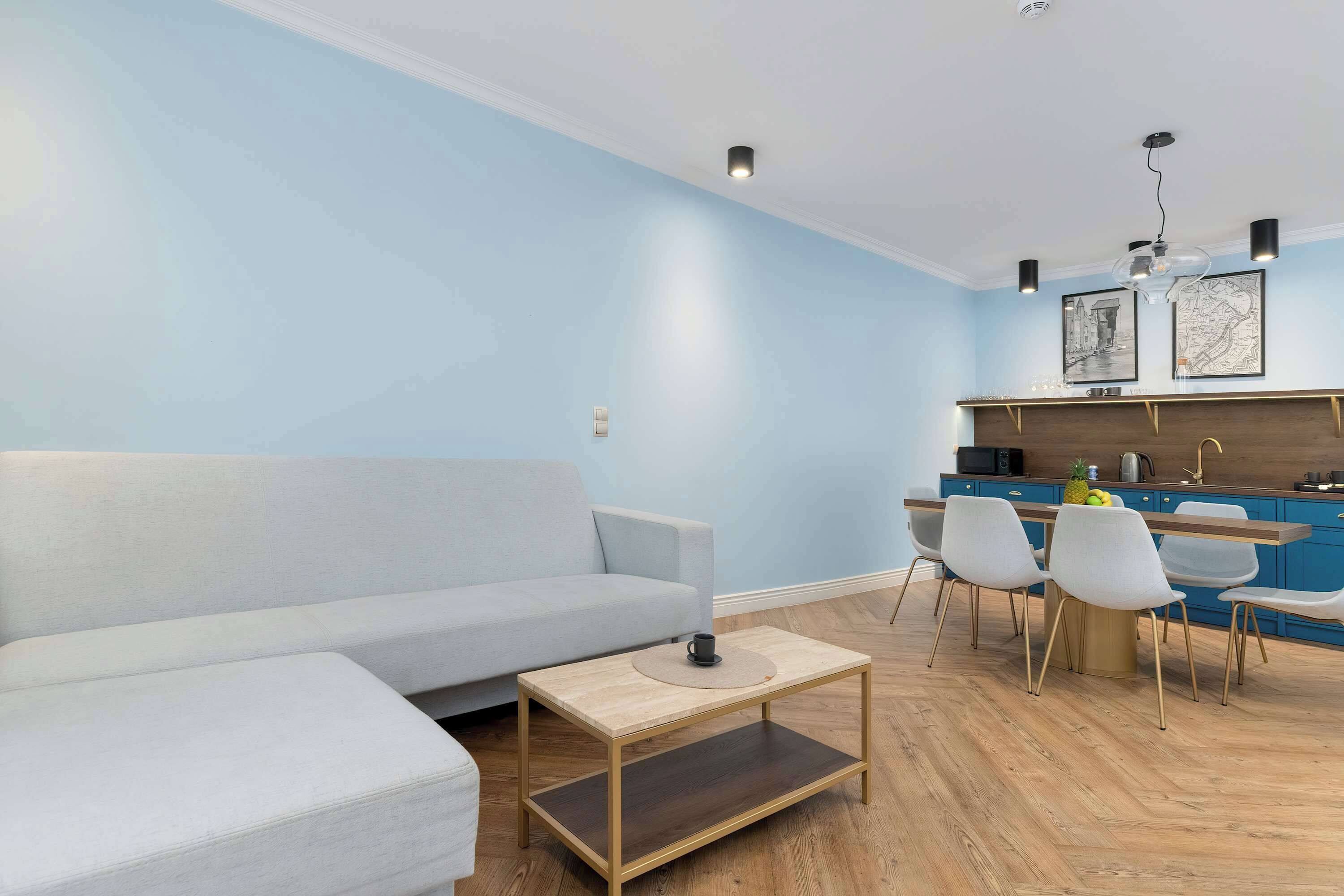 Ein modernes Wohnzimmer mit einer Couch, einem Couchtisch und einem Essbereich mit Stühlen, im Hintergrund eine Küche.