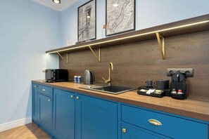 Eine moderne Küche mit blauen Schränken, einer Holzarbeitsplatte, einer Spüle, einer Kaffeemaschine und einem Wasserkocher.