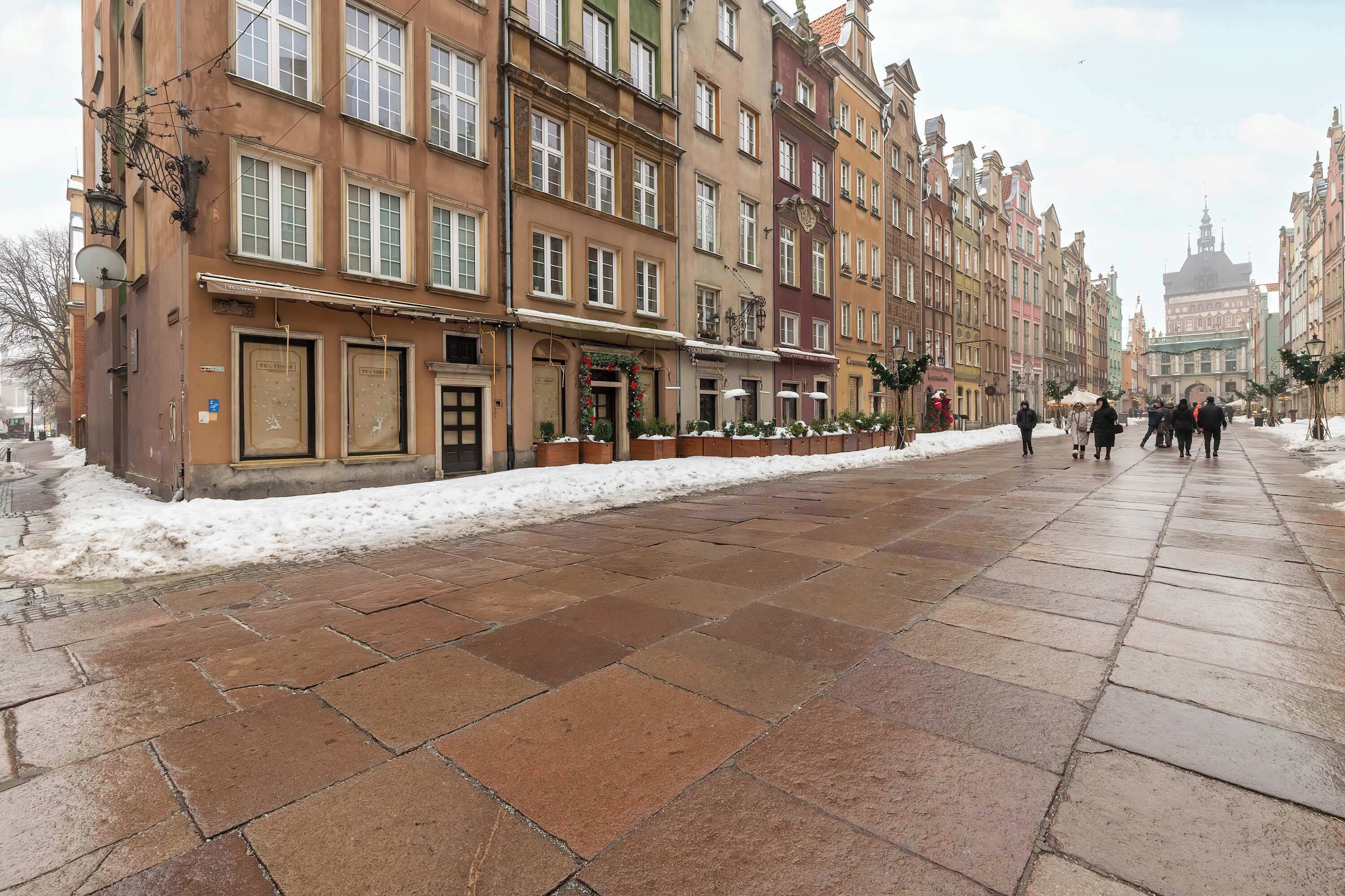 En historisk europeisk gata med fler våningar höga byggnader, kullerstenar och en snötäckt trottoar.