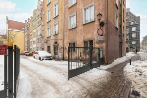 A snow-covered street with a building featuring a black gate and a sign indicating a no parking zone. - Elegant Apartment in the Heart of Gdansk | Two Bedrooms (Gdańsk)