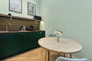 A kitchen with dark green cabinets, a round marble table, and a vase with flowers. - Artistic Studio in the Heart of Gdansk | Close to Neptune's Fountain (Gdańsk)