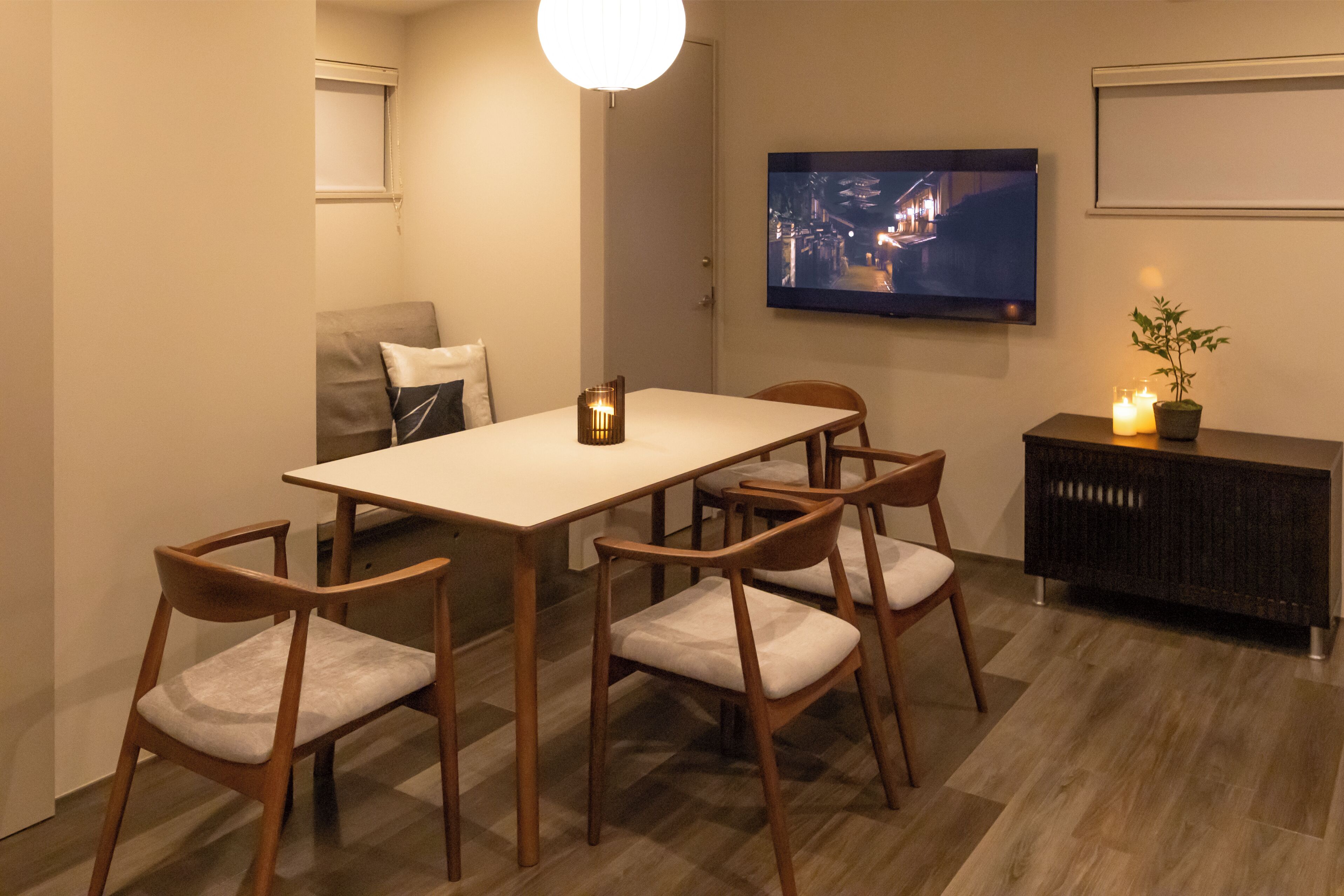 Un coin repas comprenant une table, des chaises, un téléviseur fixé au mur, un petit meuble et une plante.
