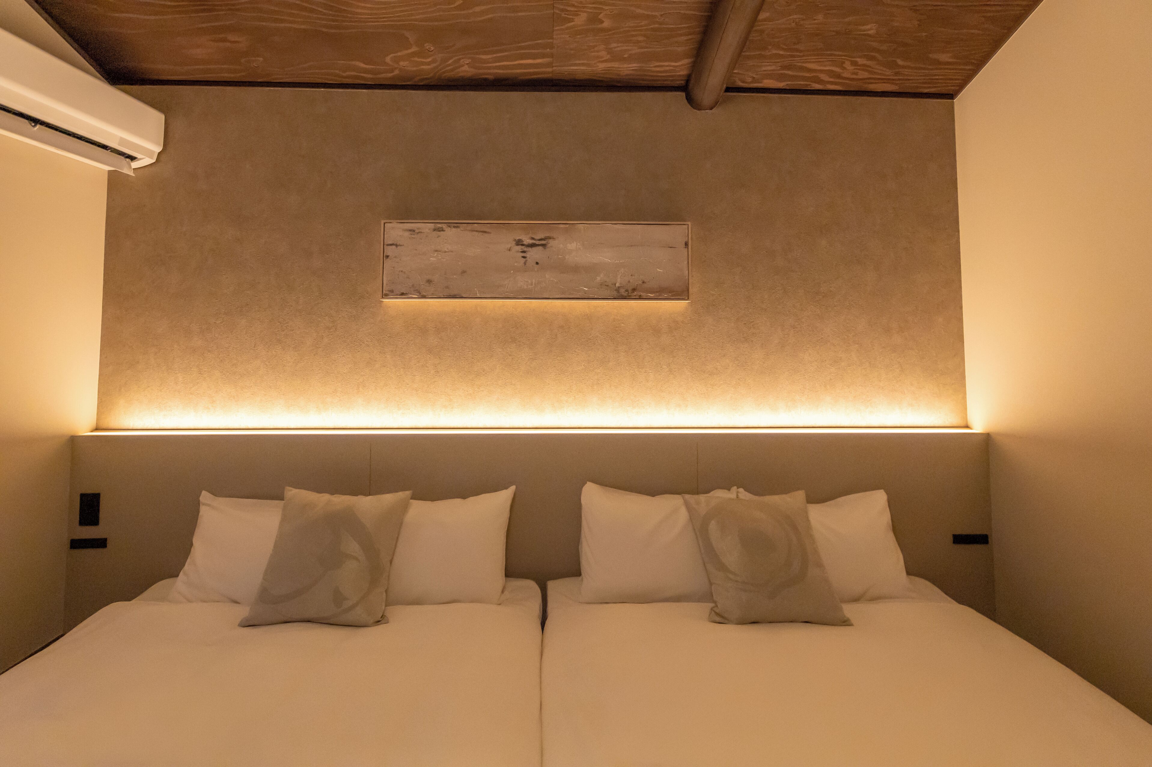 A hotel room with a bed, two pillows, a headboard, and a wall-mounted light fixture.