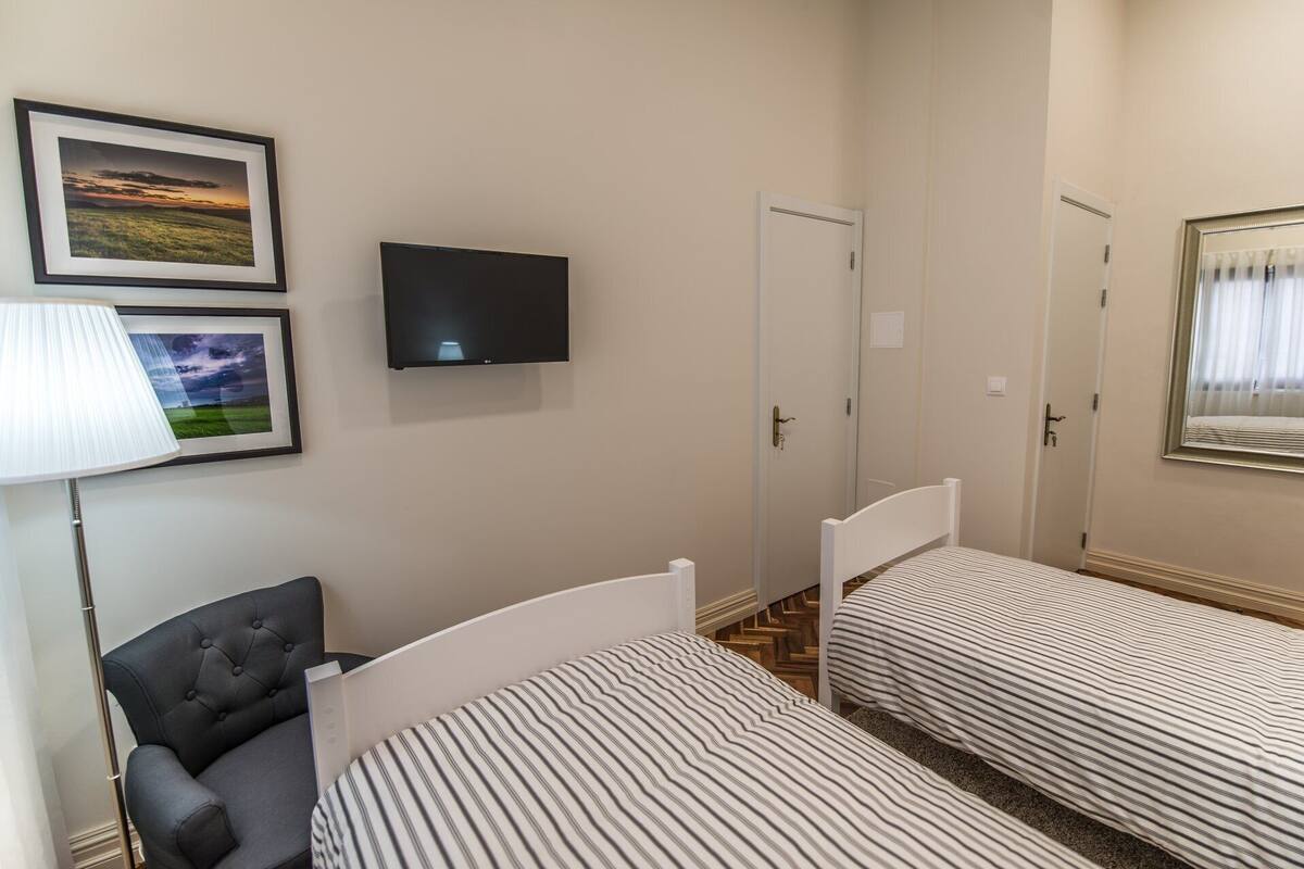 A bedroom with two beds, a TV, and a chair.