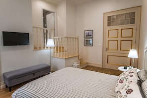 Een slaapkamer met een bed, een bankje, een televisie, een deur met ruiten en een trap.