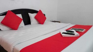 Un lit bien fait, recouvert d’une couverture blanche et rouge, avec deux oreillers rouges et un plaid rouge.