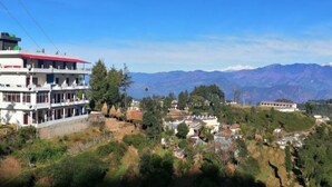 Un immeuble à plusieurs étages doté de balcons, entouré d’un paysage vallonné et avec des montagnes en arrière-plan.