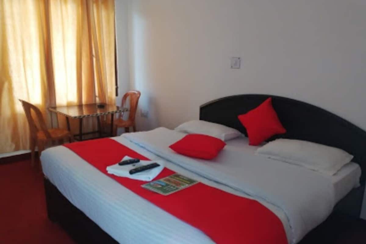 A hotel room with a bed, red pillows, a red blanket, a chair, and a table.