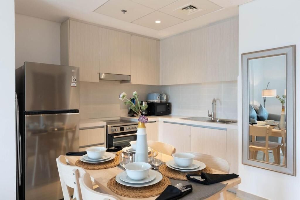 A modern kitchen with a stainless steel refrigerator, microwave, and oven. There is a dining table set with plates, bowls, and a vase of flowers.