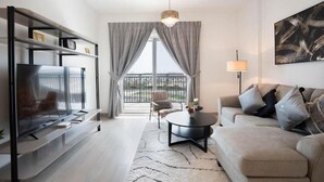 A modern living room with a flat-screen TV, a sofa, a coffee table, and a bookshelf. - Bloomfields Iconic 1BR Waters Edge (Abu Dhabi)