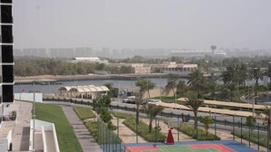 A basketball court with a red and green surface, surrounded by a fence and palm trees. - Bloomfields Iconic 1BR Waters Edge (Abu Dhabi)