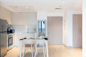 Una cocina moderna con armarios blancos, un refrigerador de acero inoxidable, una cafetera y un comedor con dos sillas blancas y una mesa.