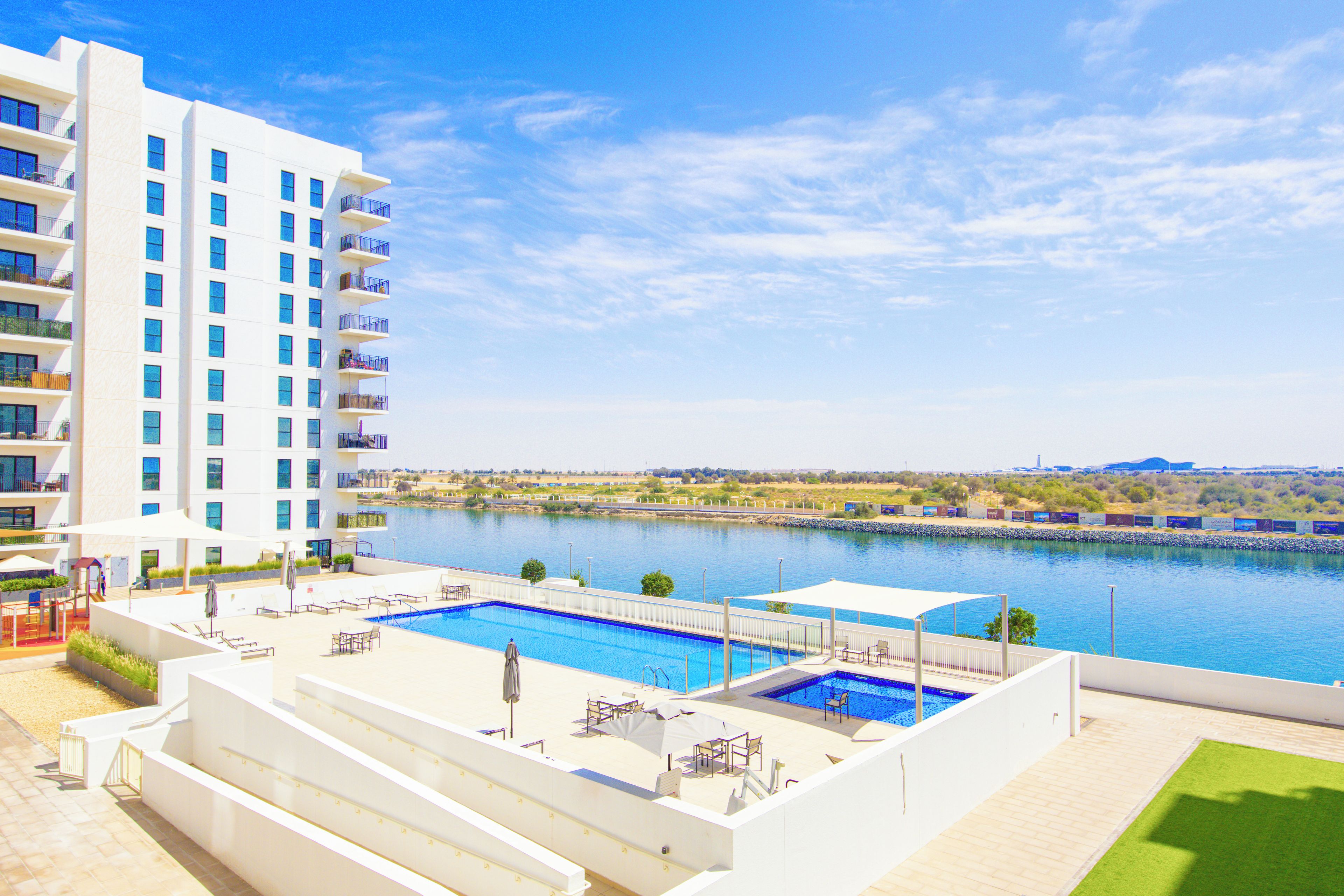 A hotel with a swimming pool, outdoor seating, and a view of a body of water.