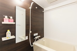 Ein modernes Badezimmer mit einer Badewanne, einer Dusche und einem Spiegel. Es gibt Ablagen mit Pflegeprodukten und eine Flasche Shampoo.