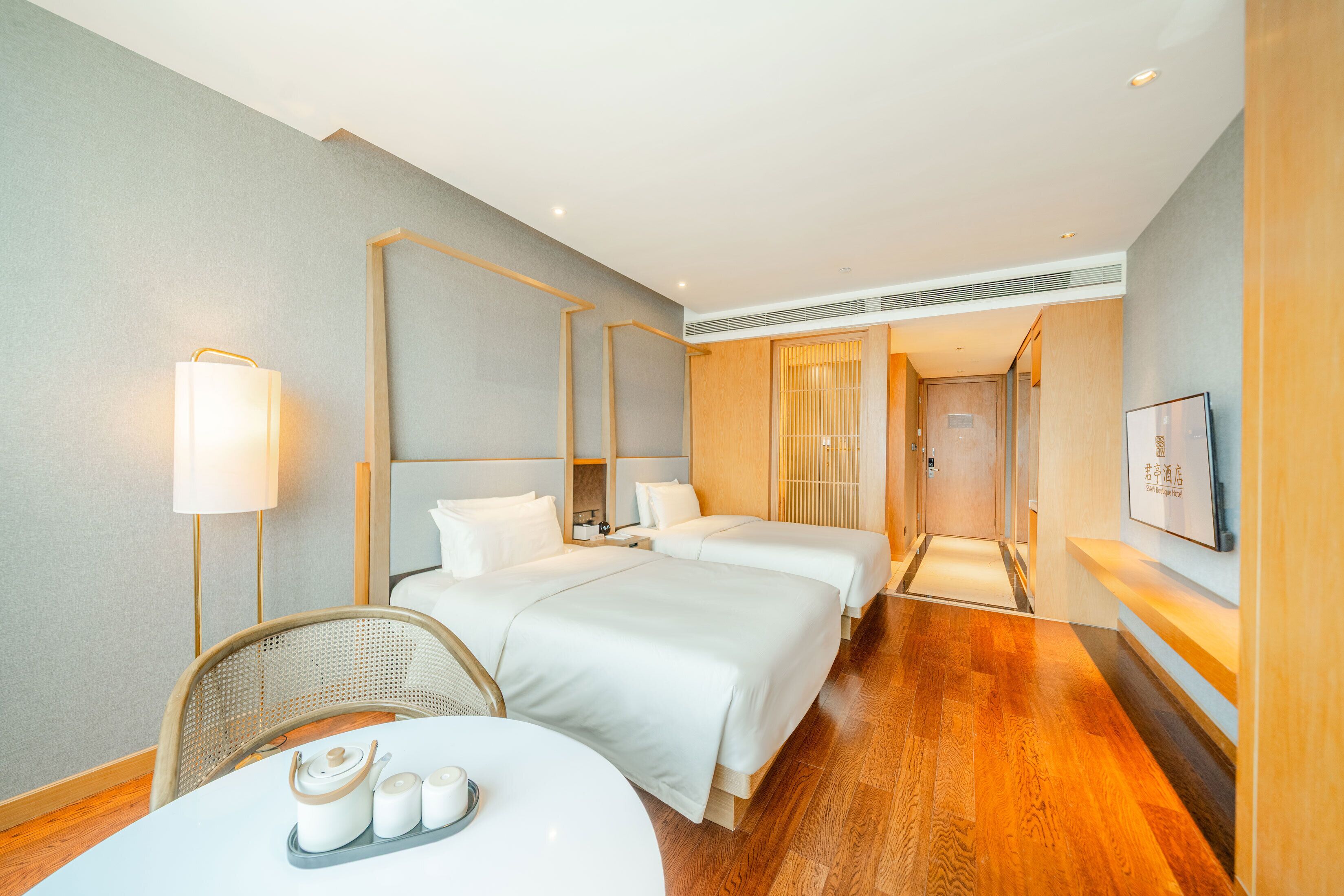 A hotel room with two beds, a dining table, a chair, a lamp, and a television.