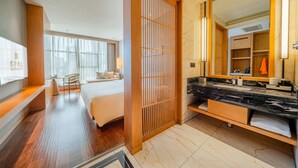 Habitación de hotel con cama, separador de madera, baño con espejo grande y televisor en la pared.