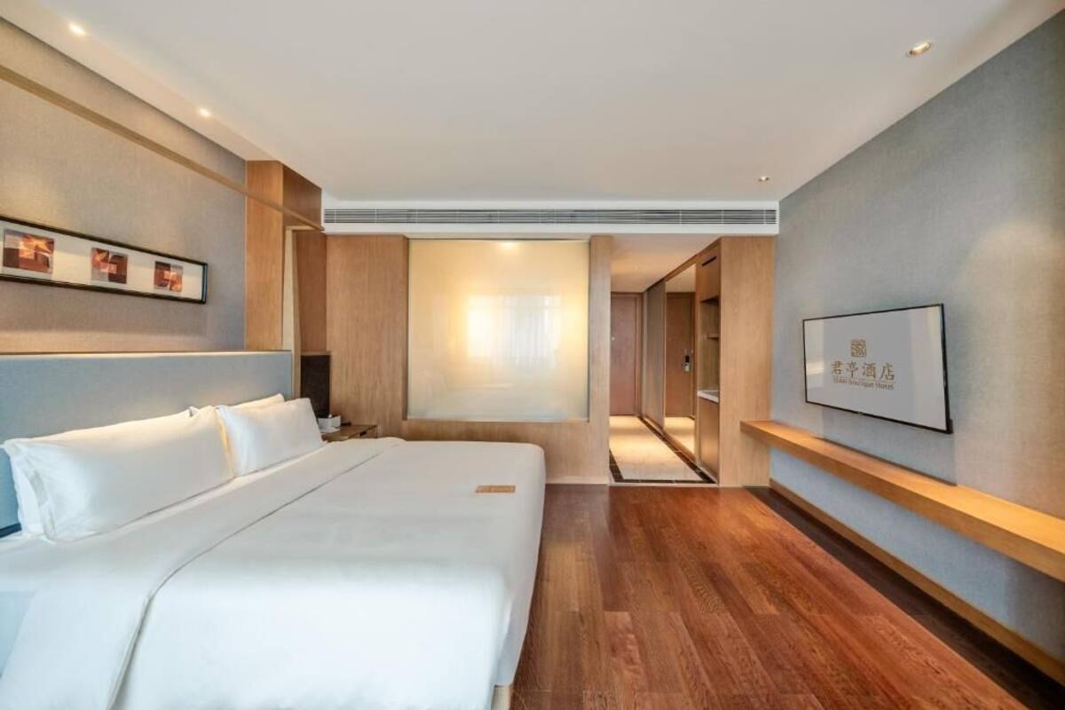 Una habitación de hotel moderna con una cama grande, suelo de madera, televisión montada en la pared y un cuadro enmarcado.