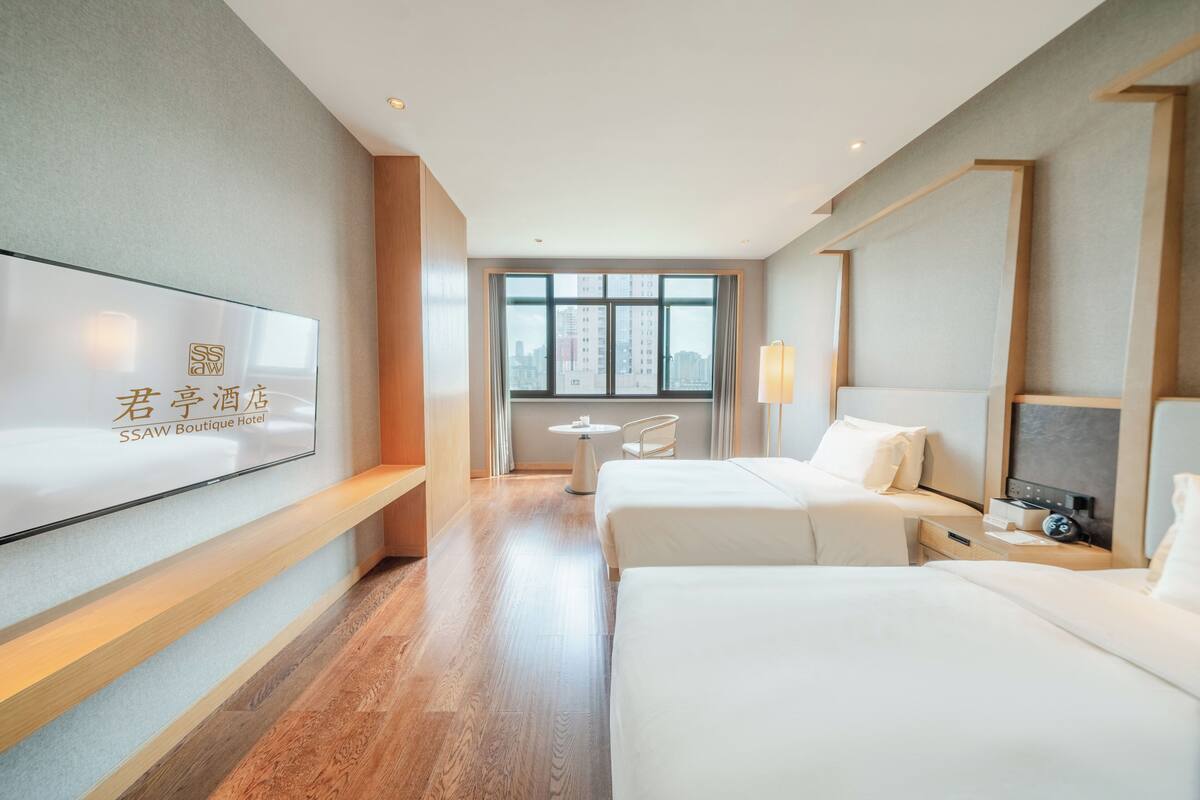 Habitación de hotel con dos camas, televisión, una mesita y ventana con vista a la ciudad.