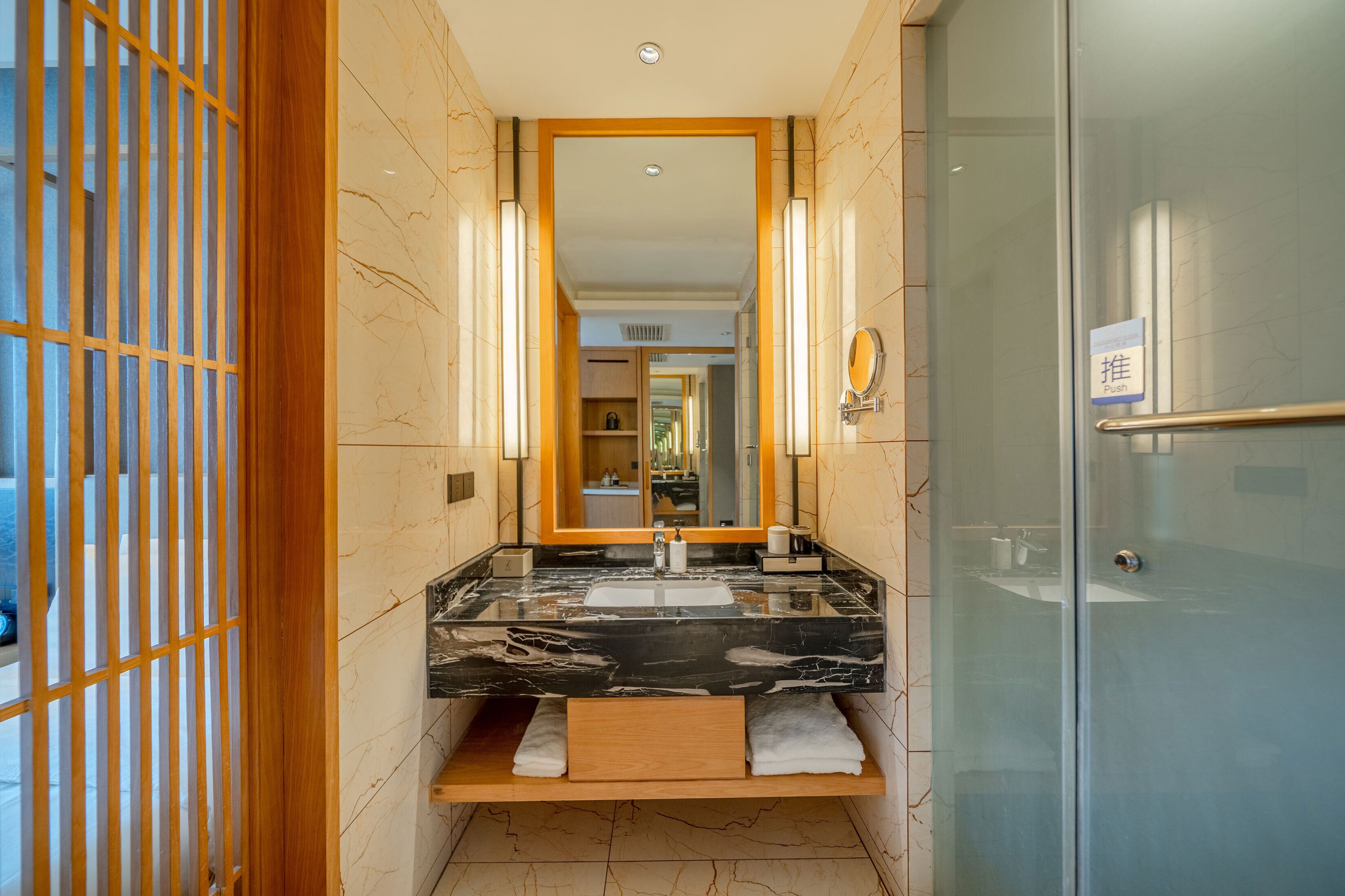 A modern bathroom with a marble sink, a large mirror, and a glass shower door.