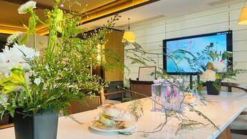 Een hotel receptie met een marmeren balie, een potplant met bloemen, een televisiescherm en een waterdispenser.