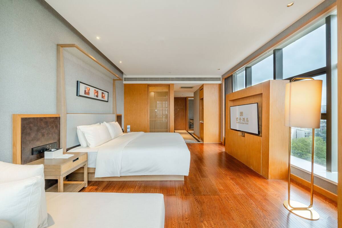 Habitación de hotel moderna con una cama grande, mesitas de noche, un escritorio y un ventanal con vistas.