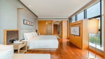 A modern hotel room with a large bed, bedside tables, a desk, and a large window offering a view.