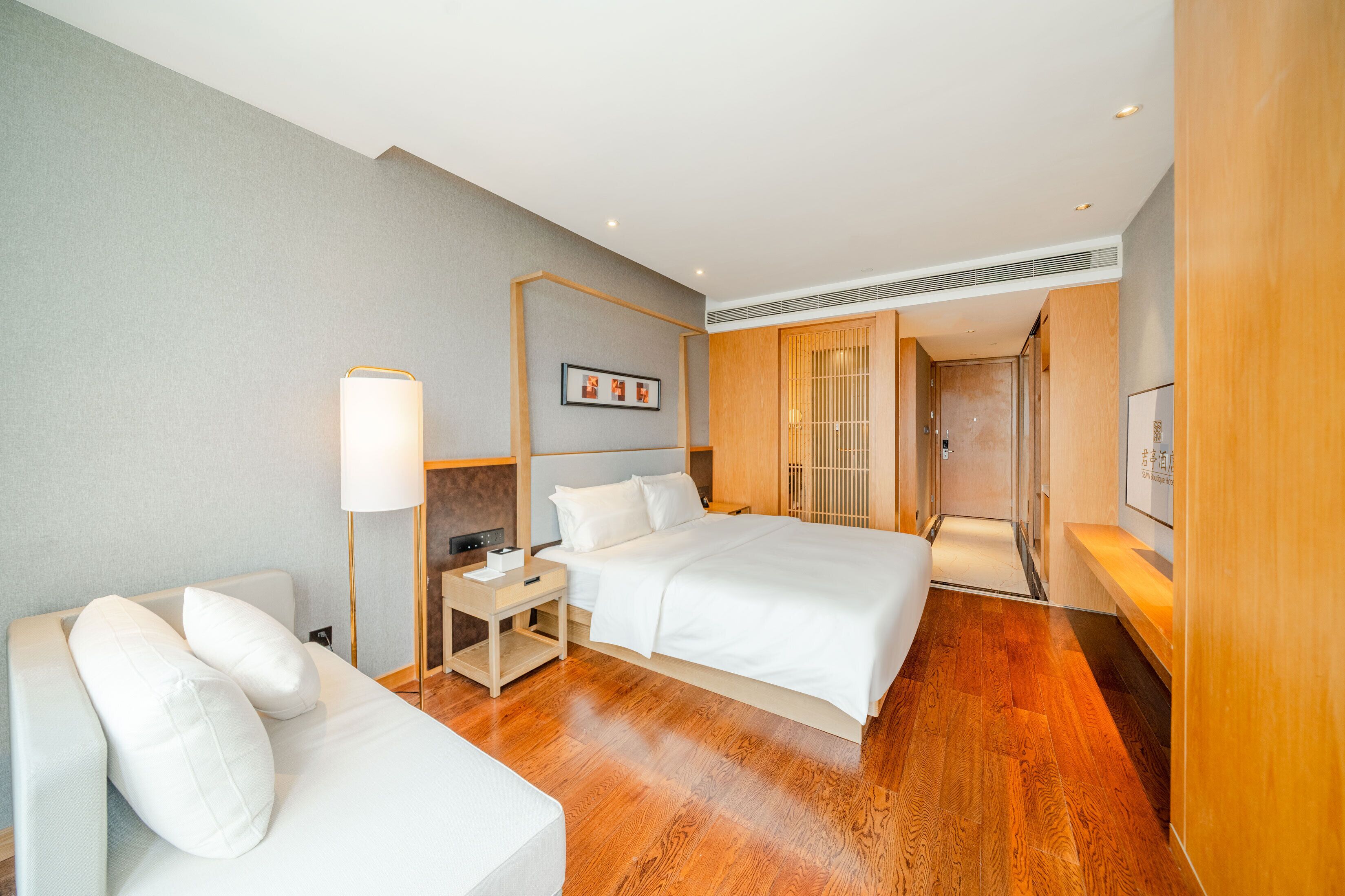 Una habitación de hotel con cama, mesitas de noche, lámpara, televisor y piso de madera.