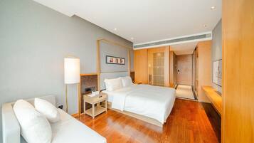Una habitación de hotel con cama, mesitas de noche, lámpara, televisor y piso de madera.