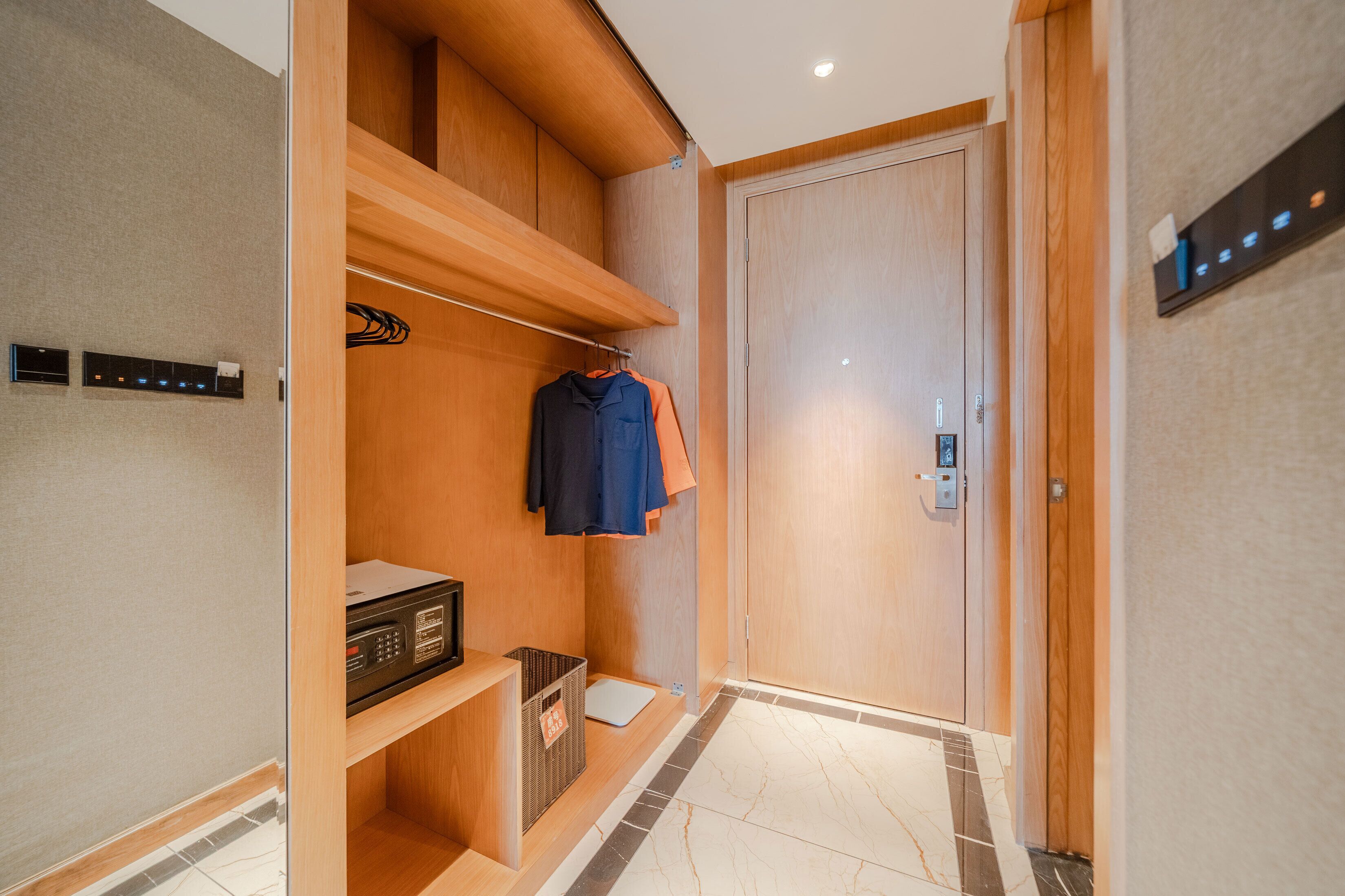 Una habitación de hotel moderna con un armario de madera, un escritorio pequeño con una radio y una puerta con cerradura digital.
