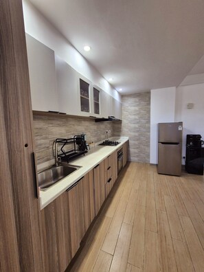 A modern kitchen with wooden cabinets, a stainless steel sink, a gas stove, and a built-in oven. - Cozy 2-bedroom fully fitted apartment in Nairobi with pool and fitness room (Kileleshwa,)