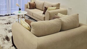 Un soggiorno moderno con un divano beige, un tavolino rotondo e un tappeto bianco. Alle pareti, due dipinti astratti e una finestra con tende leggere.