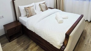 Un letto rifatto con cura, con struttura in legno e biancheria bianca, un comodino in legno e una finestra con tende.
