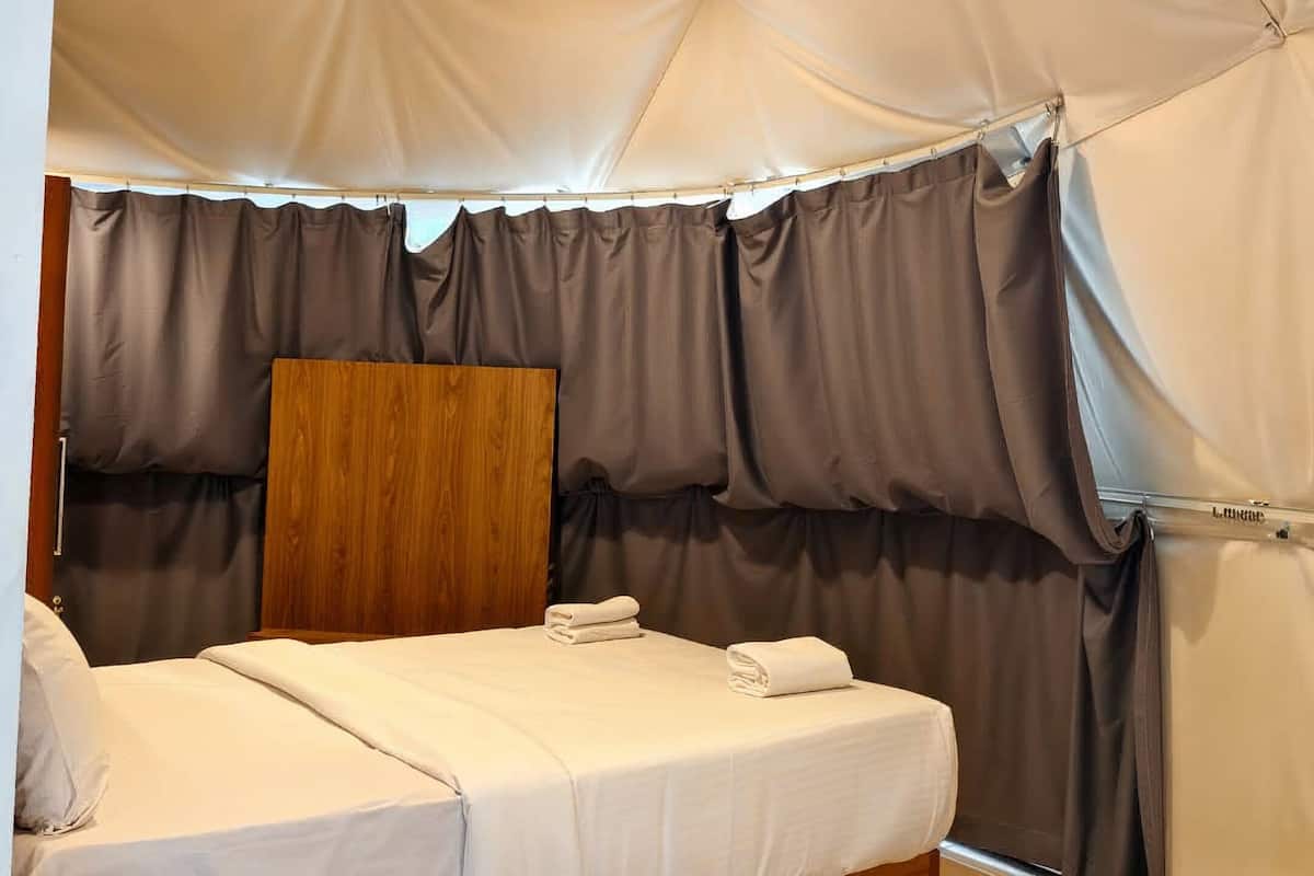 Een tentkamer met een bed, een houten paneel en een raam met gordijnen.