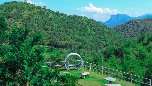 Un paysage verdoyant et luxuriant, avec une structure métallique circulaire au premier plan, entourée de bancs et d’une rambarde.