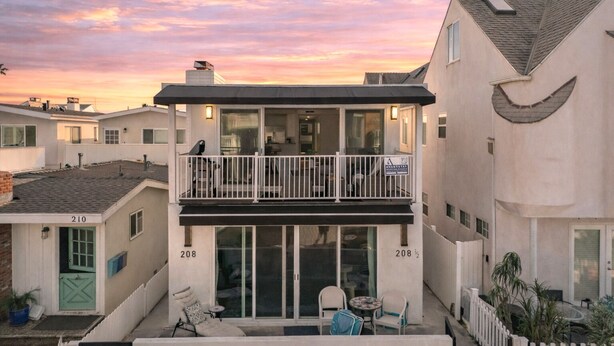 A two-story residential building with a balcony, large windows, and a view of the sunset. - Top-Floor West Newport Retreat | Balcony | Near Beach + Cafes | Seabright Sky (Newport Beach)