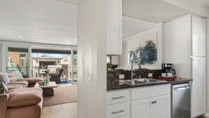A modern kitchen with white cabinets, a granite countertop, and a dishwasher. - Top-Floor West Newport Retreat | Balcony | Near Beach + Cafes | Seabright Sky (Newport Beach)