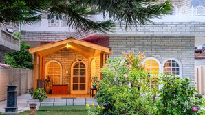 A brick house with a wooden porch, arched windows, and a small garden. - White House By Kulut (Kullu)
