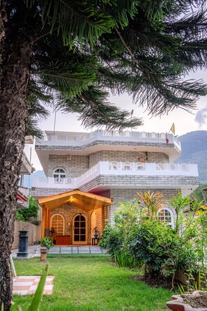 A two-story building with a balcony, a wooden porch, and a well-maintained garden. - White House By Kulut (Kullu)