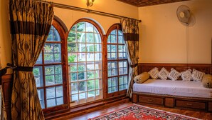 A room with a bed, a large window with curtains, a fan, and a patterned rug. - White House By Kulut (Kullu)