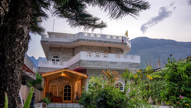 A multi-story building with a balcony, a front entrance, and a garden with various plants. - White House By Kulut (Kullu)