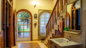 A bathroom with a large sink, wooden cabinets, a mirror, and a view of a garden through a door. - White House By Kulut (Kullu)