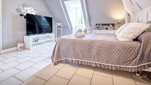 Un dormitorio moderno con una cama grande, televisión y un mueble blanco para guardar objetos.