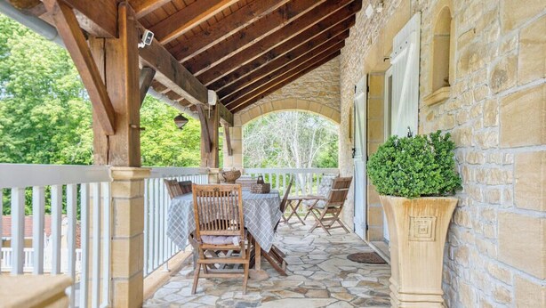 Un patio techado al aire libre con suelo de piedra, mobiliario de madera y una planta en maceta.